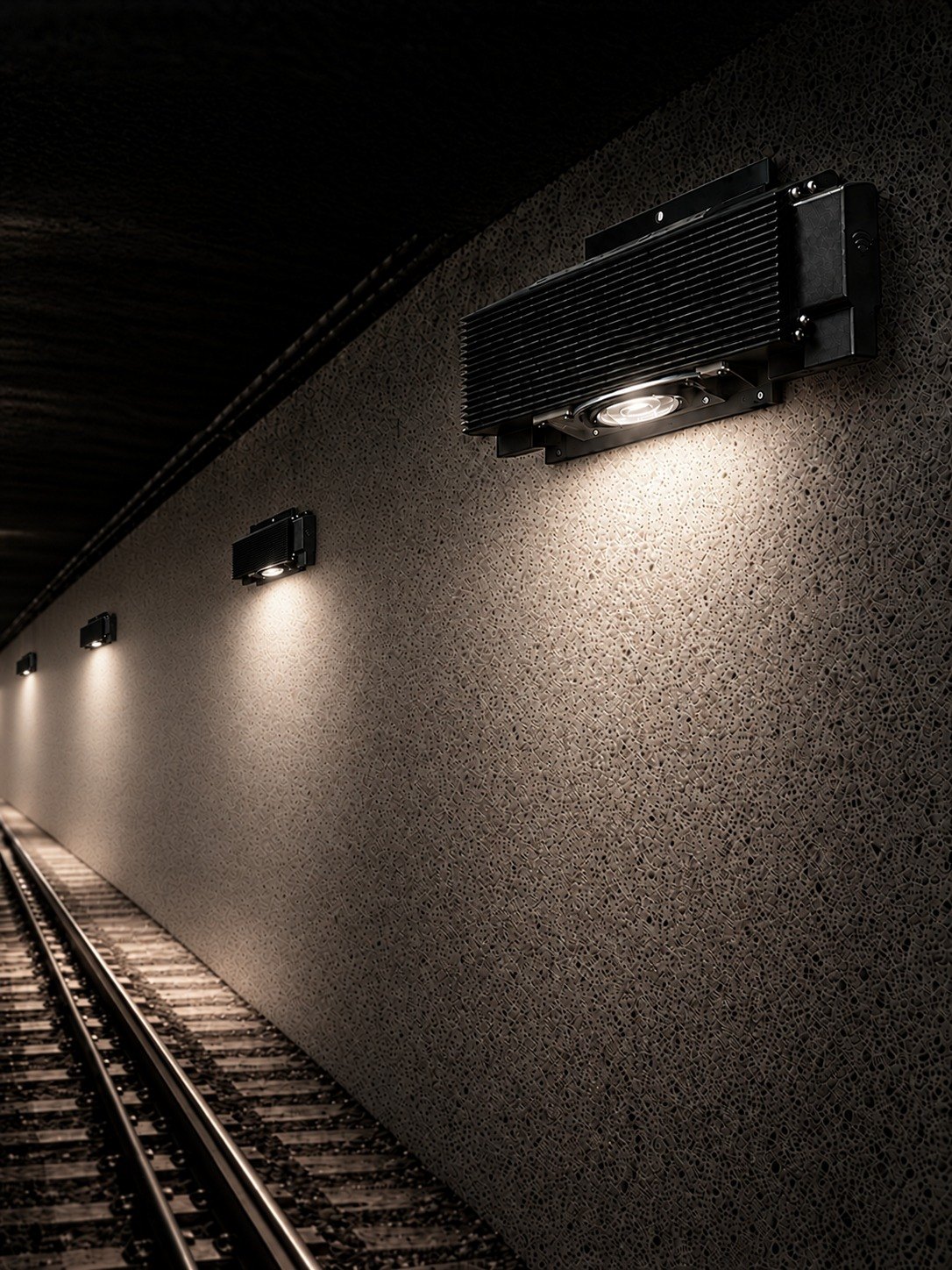 MTLx Pro tunnel fixture mounted on a concrete tunnel wall, downlight lit, with the walkway and track below